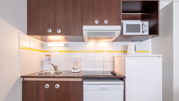 A compact kitchen with wooden cabinets, a microwave, a coffee maker, and a dishwasher. - Comfort Aparthotel Les Hauts d'Annecy (Annecy)