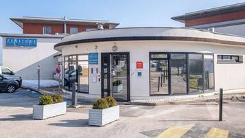 A hotel entrance with a reception desk, a sign for 'Les Hauts D'Ancey,' and a parking area with a car.