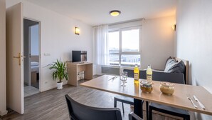 A modern dining area with a wooden table, chairs, a potted plant, and a television in the background. - Comfort Aparthotel Les Hauts d'Annecy (Annecy)
