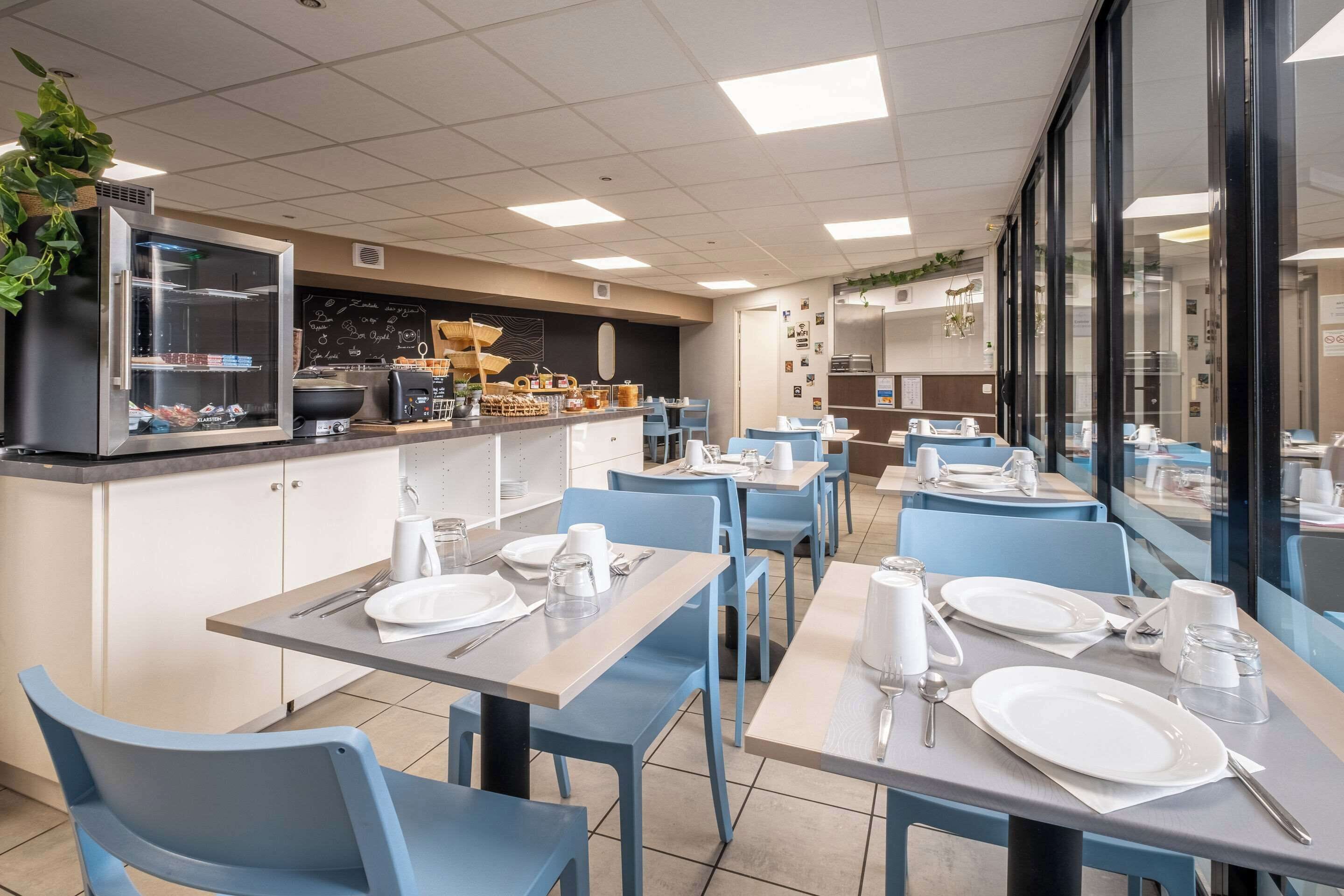 A restaurant with blue chairs and tables, a kitchen area with cooking equipment, and a chalkboard menu.