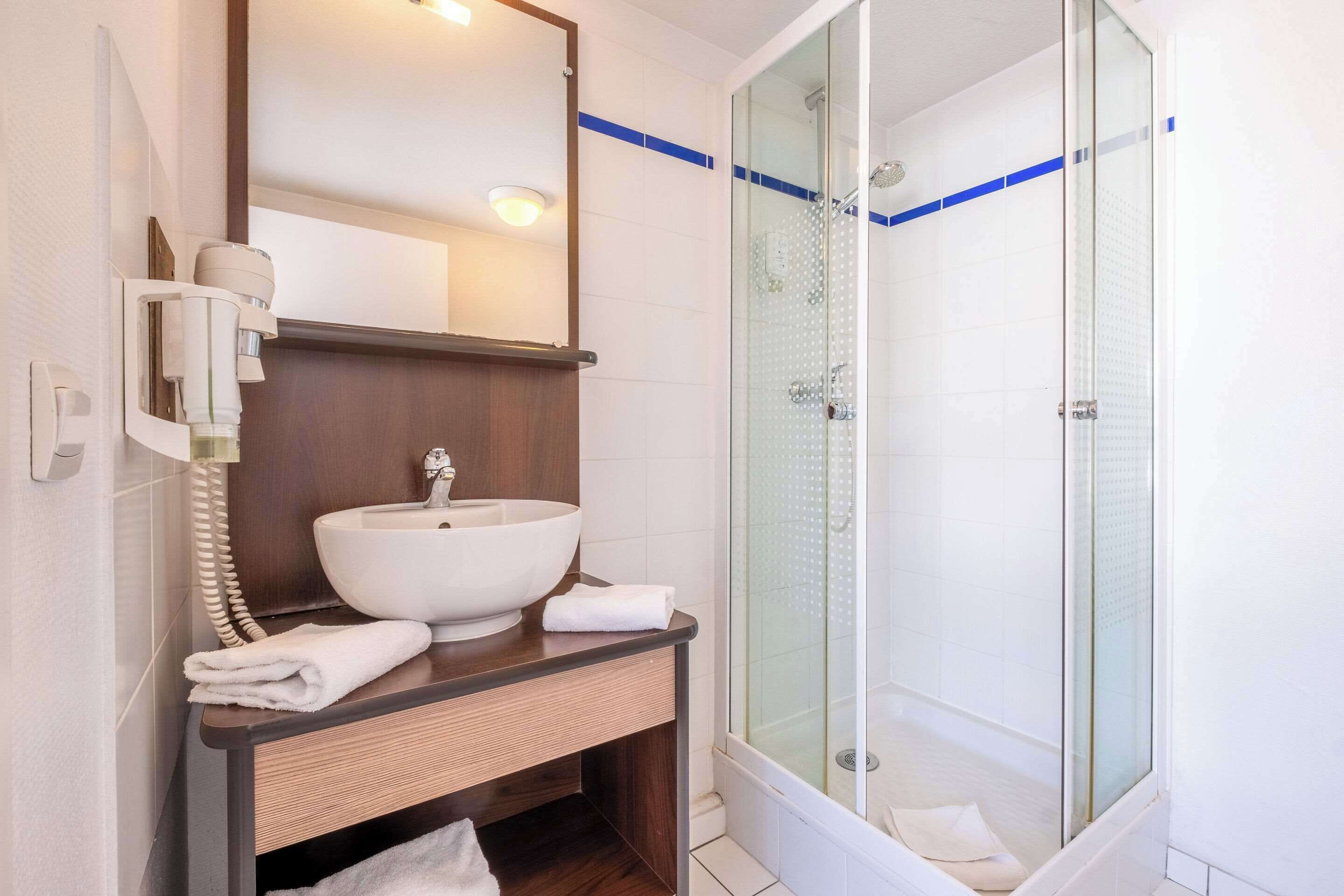 A bathroom with a large white sink, a mirror, a telephone, and a glass-enclosed shower.