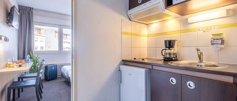 Cocina de hotel compacta con microondas, cafetera y un refrigerador pequeño.