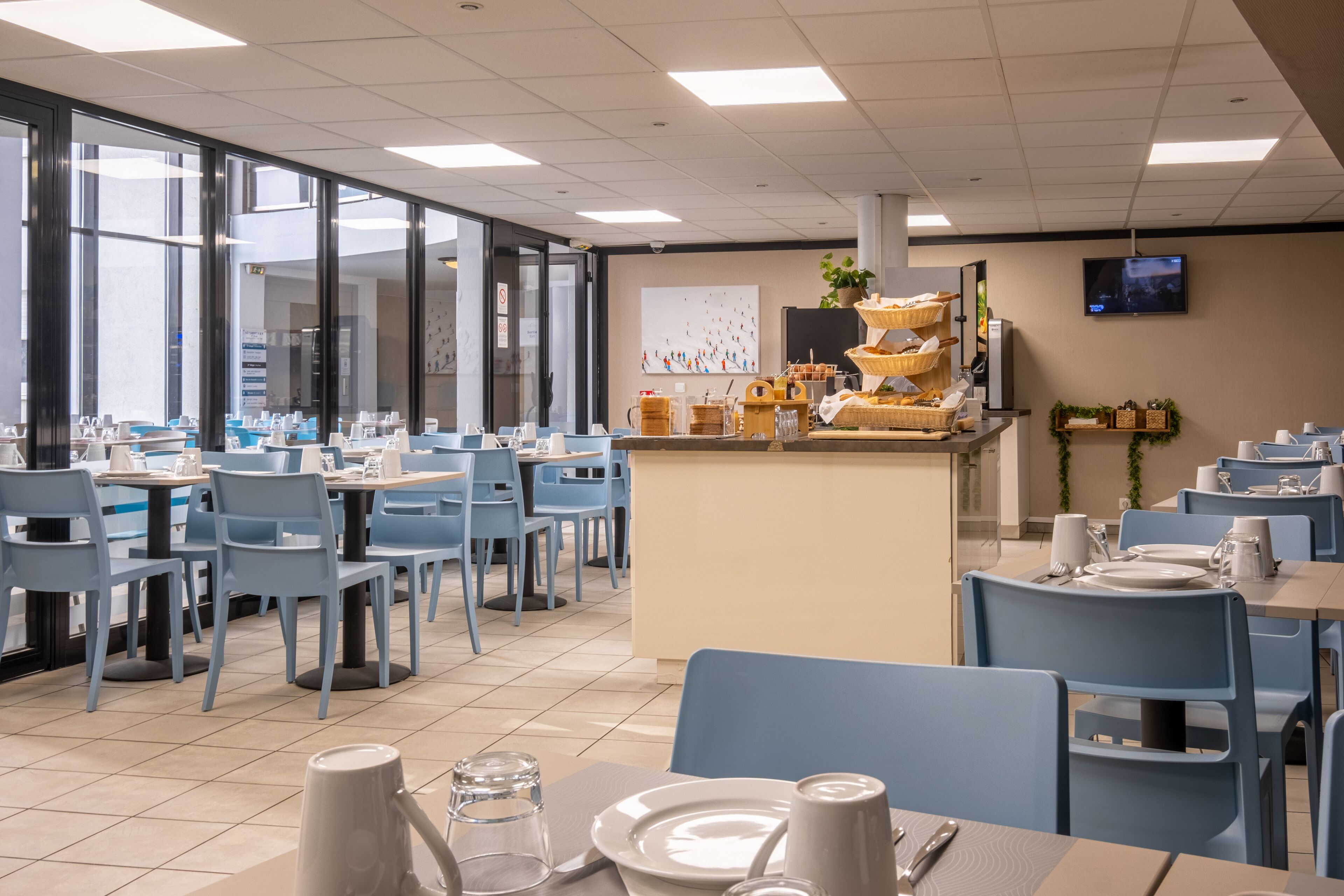 Un comedor moderno con sillas y mesas azules, una barra central con cestas y un televisor en la pared.