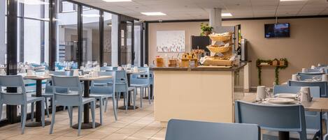 A modern dining area with blue chairs and tables, a central counter with baskets, and a television on the wall.