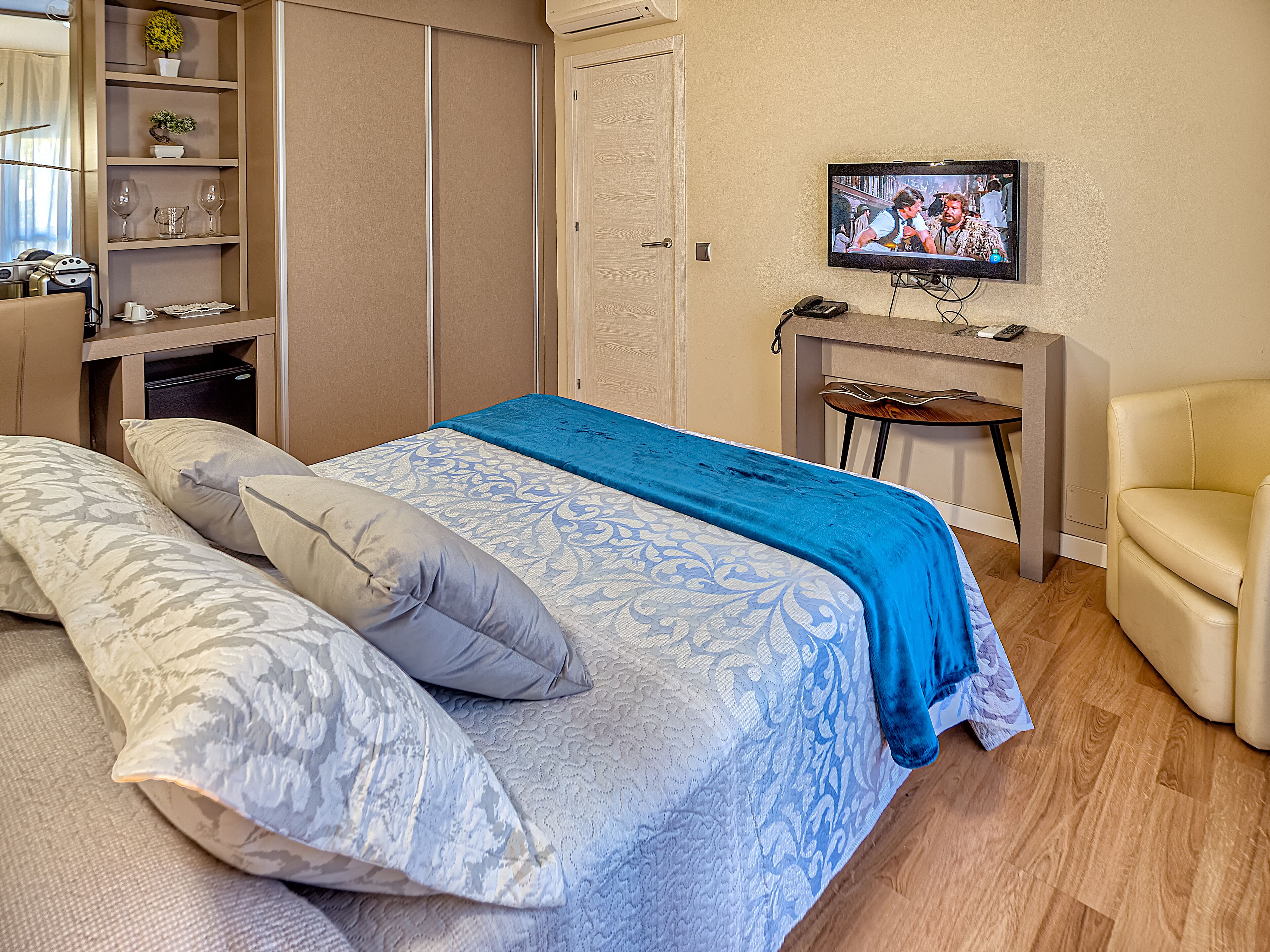 A bedroom with a bed, pillows, a TV, a desk, and a chair.