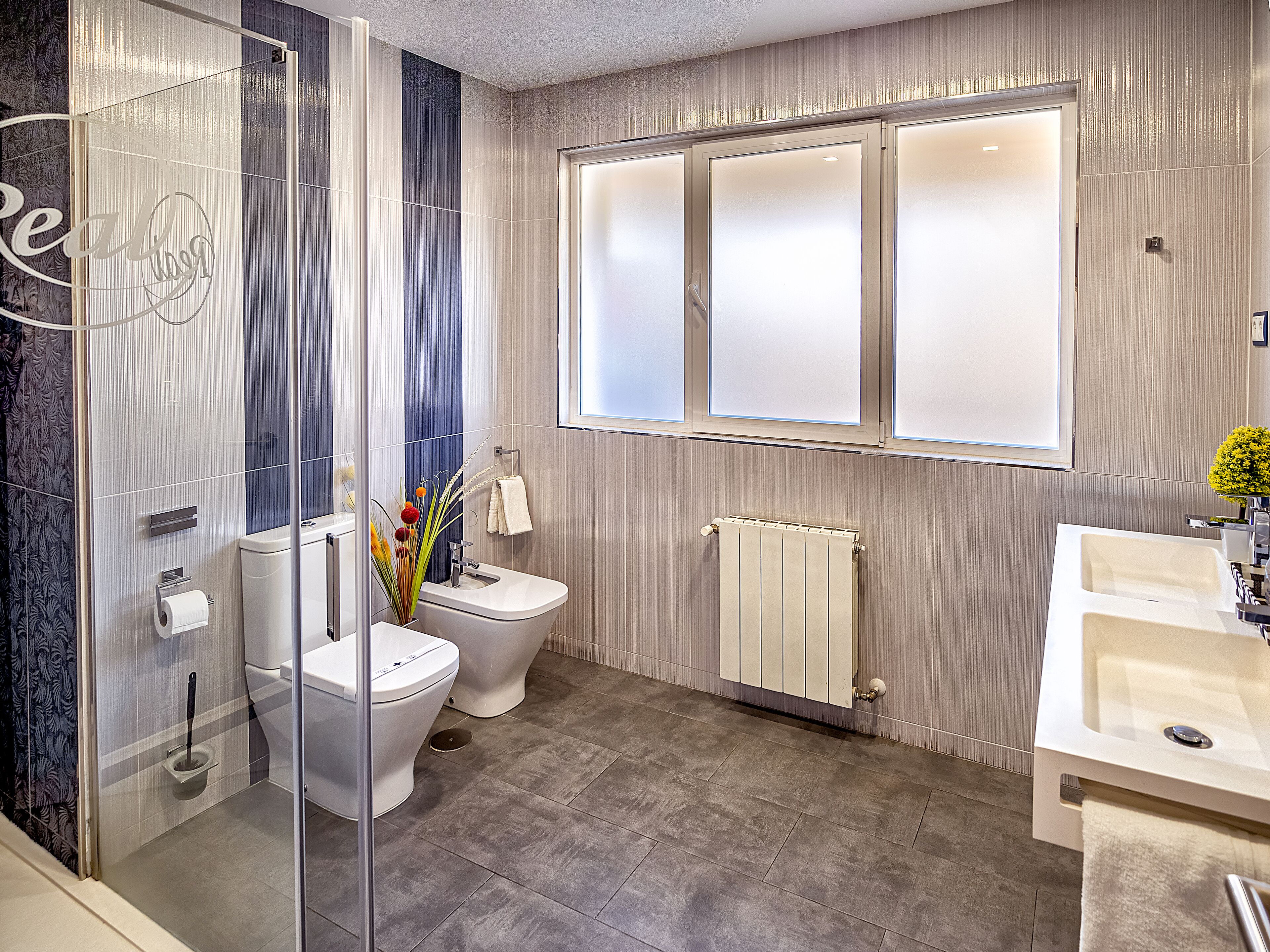 A modern bathroom with a glass shower enclosure, a toilet, a bidet, and a sink.