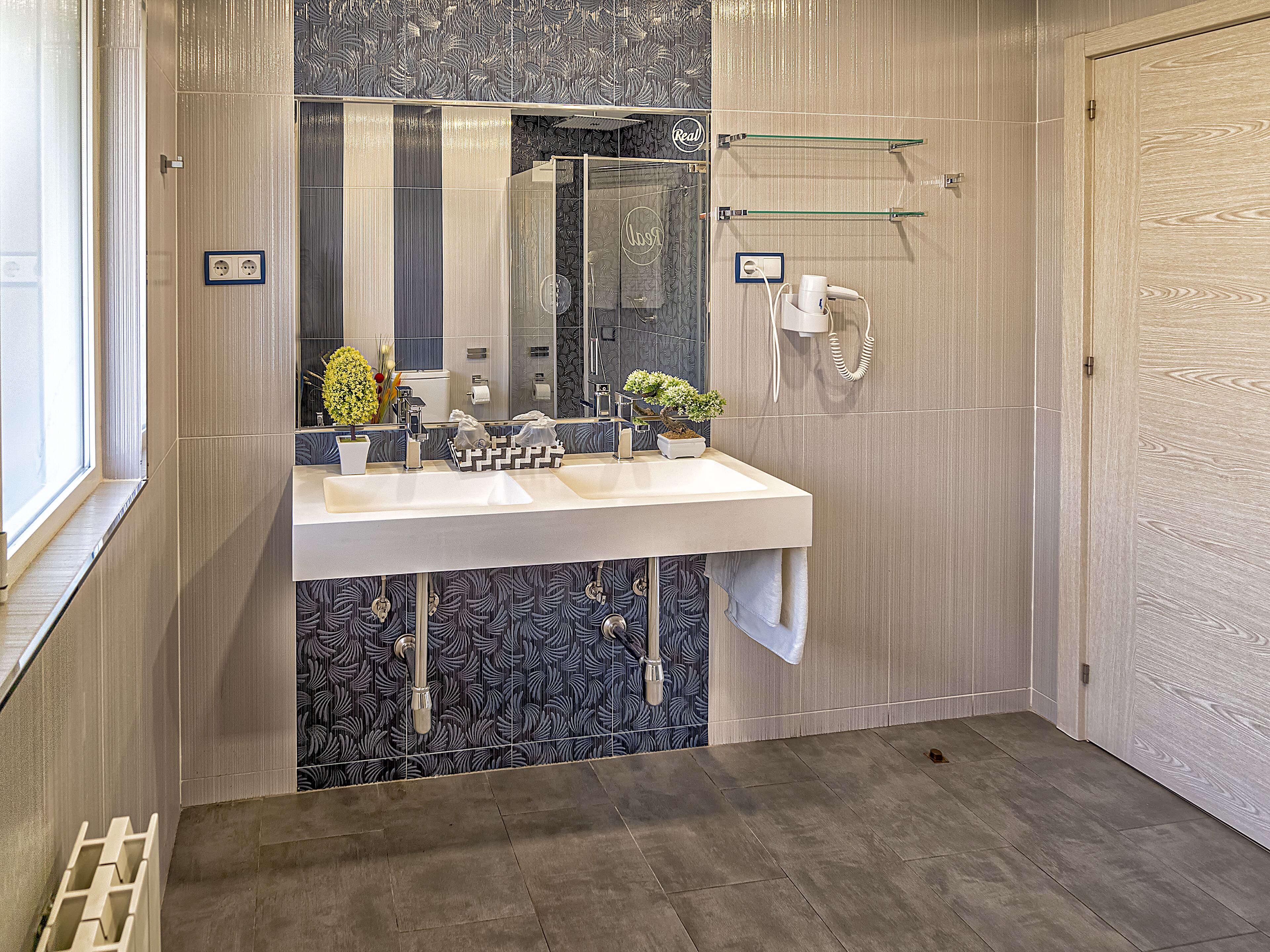 Een moderne badkamer met een grote spiegel, twee wasbakken, een handdoekrek en een douche.