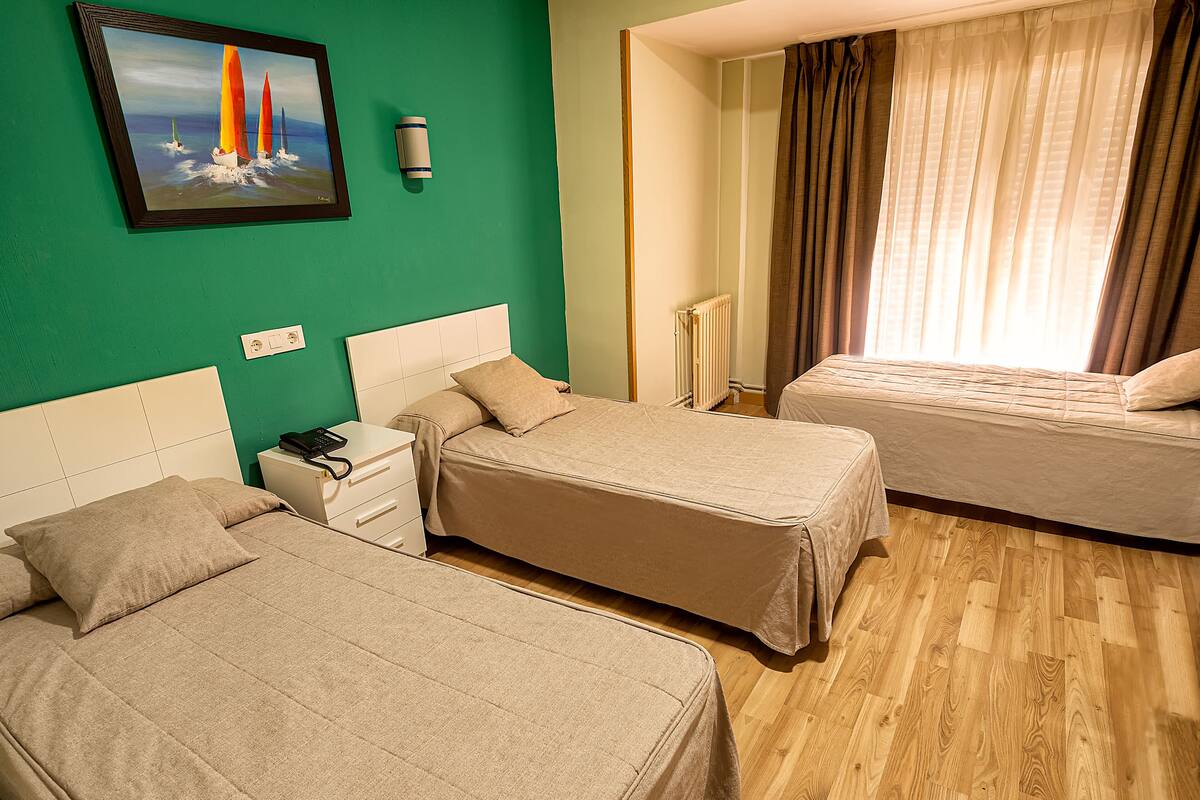 A hotel room with two beds, a nightstand, a telephone, a painting, and a window with curtains.