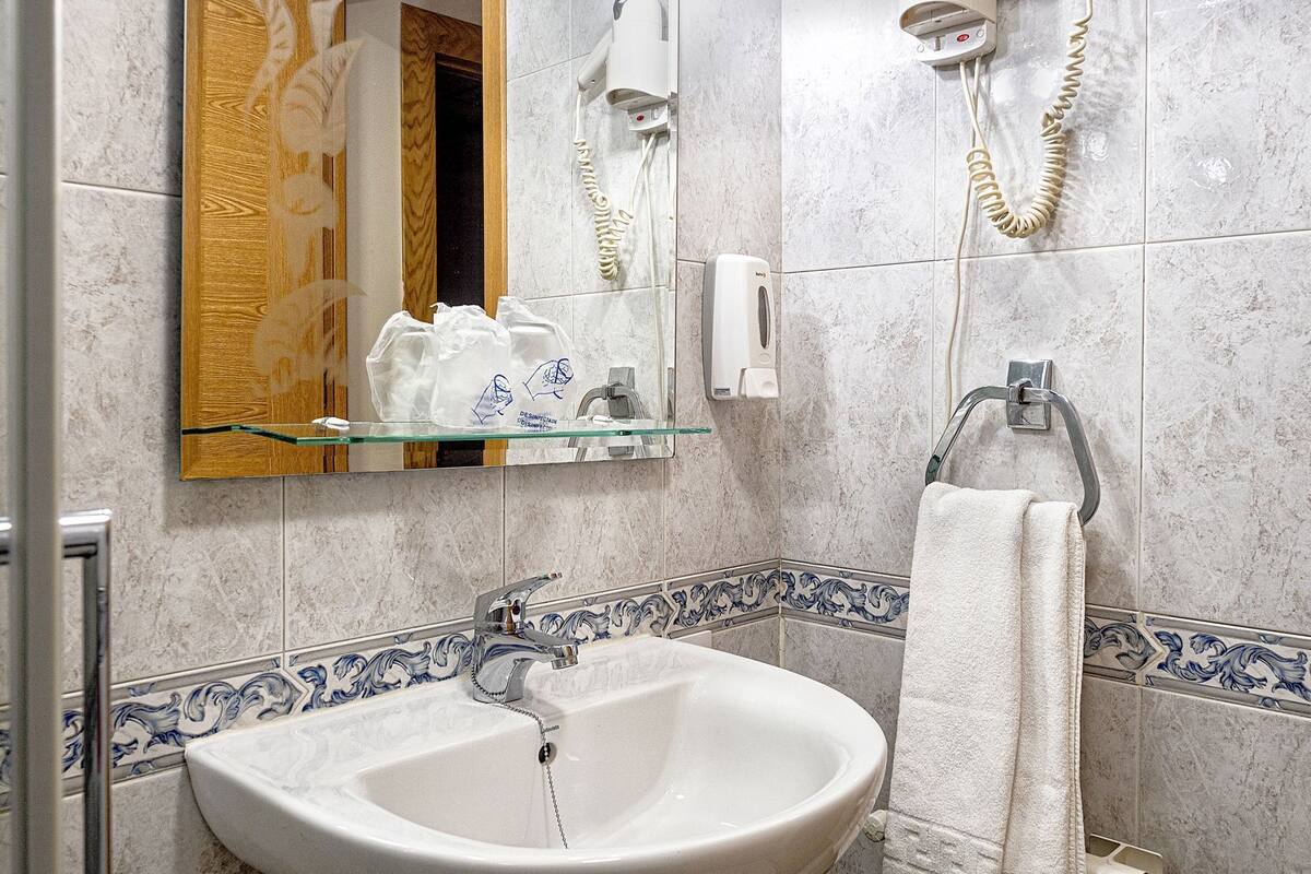 A bathroom with a sink, mirror, hairdryer, and towel rack.