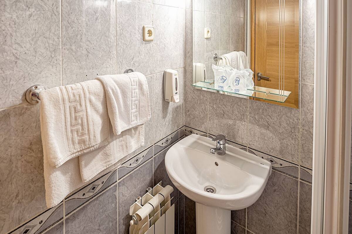 A bathroom with a marble wall, a white sink, a towel rack, a glass shelf with toiletries, and a mirror.