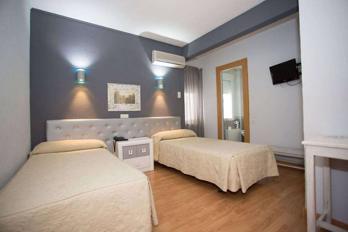 A hotel room with two beds, a nightstand, a mirror, and an air conditioning unit.