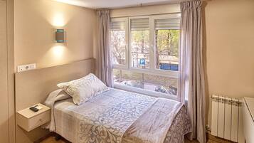 A bedroom with a bed, a nightstand, a window with curtains, and a radiator.
