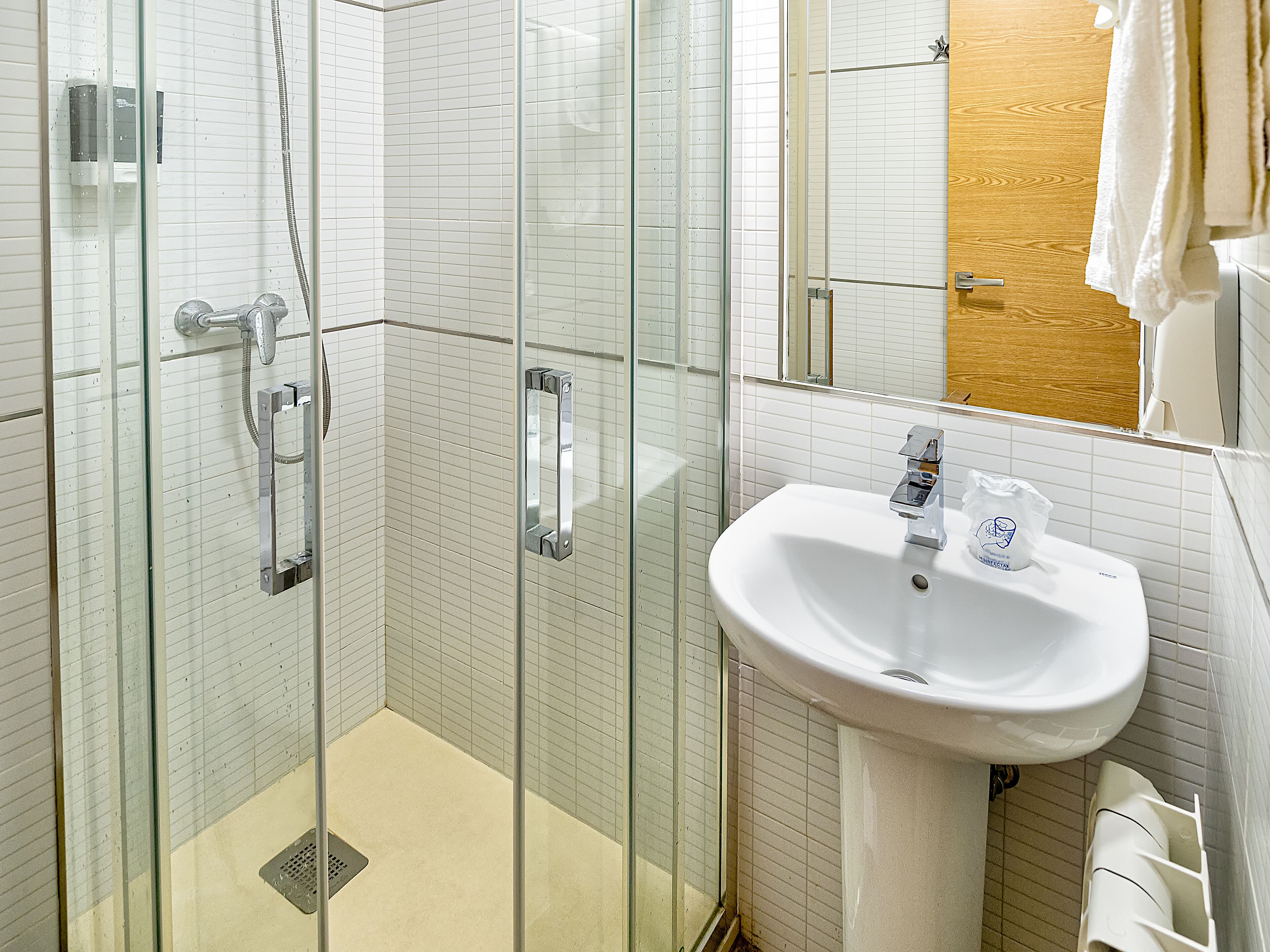 A bathroom with a glass-enclosed shower, a white sink, and a wooden door.