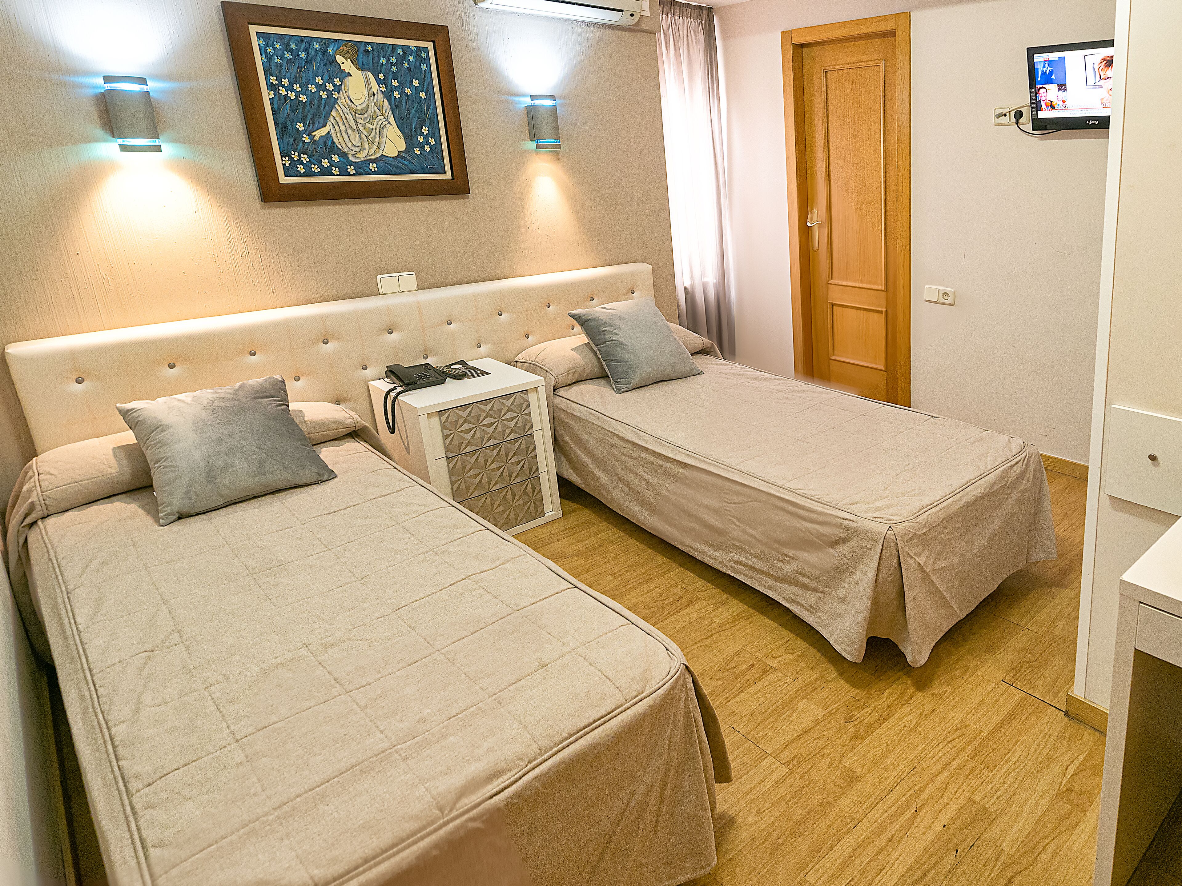 Una camera da letto con due letti singoli, un comodino con il telefono, una lampada a parete e un quadro.