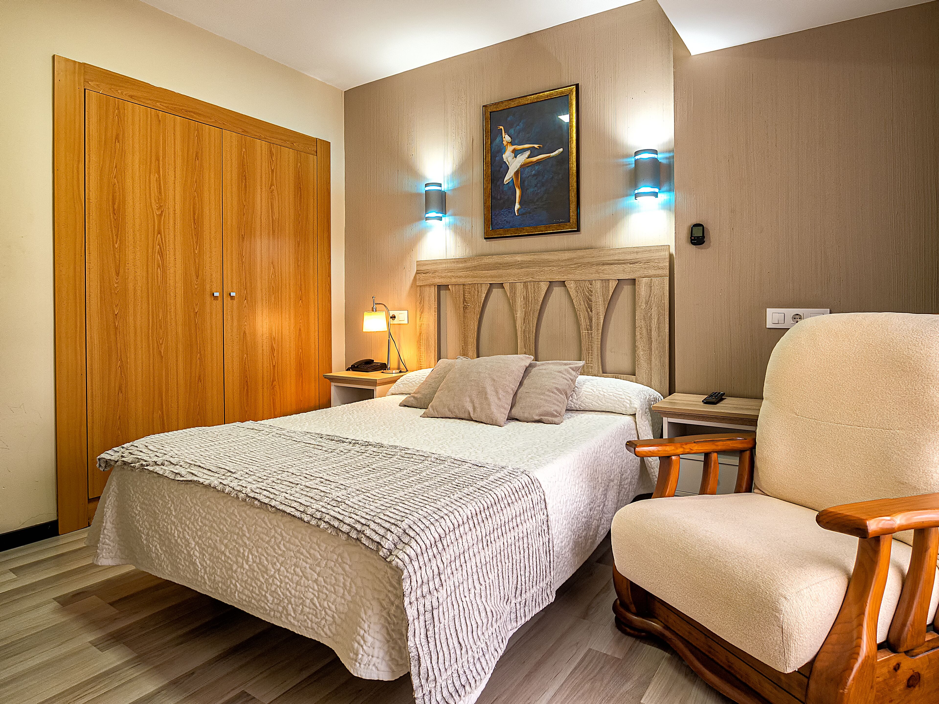 Un dormitorio con una cama grande, un armario de madera, una mesita de noche con lámpara y una silla.