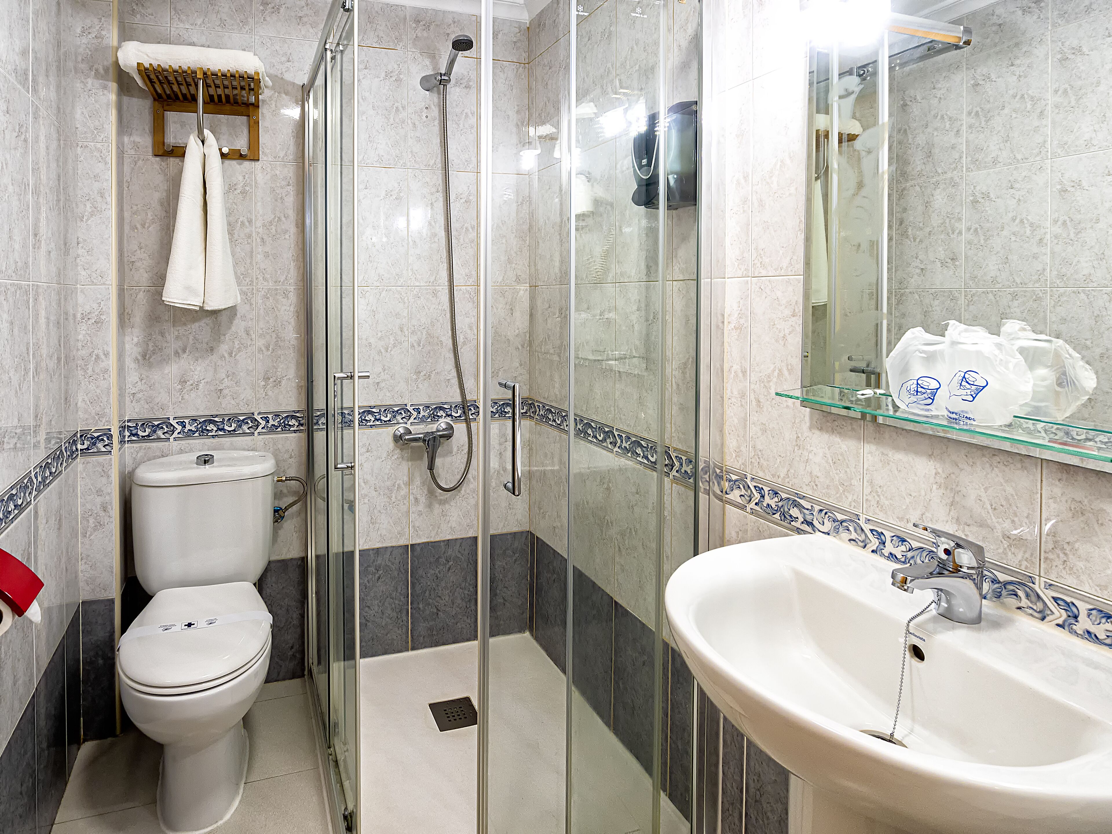 Un baño con ducha de vidrio, inodoro y lavamanos con espejo superior.