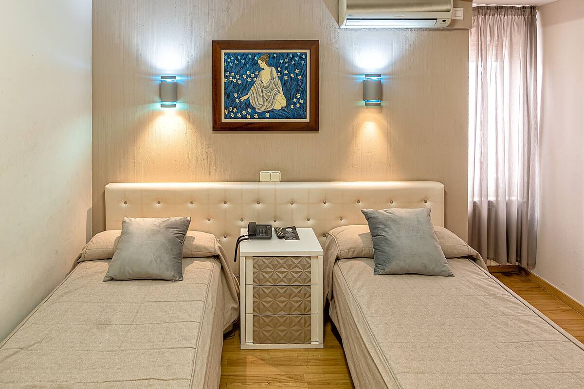 A twin room with two beds, a bedside table with a phone, and a painting on the wall.