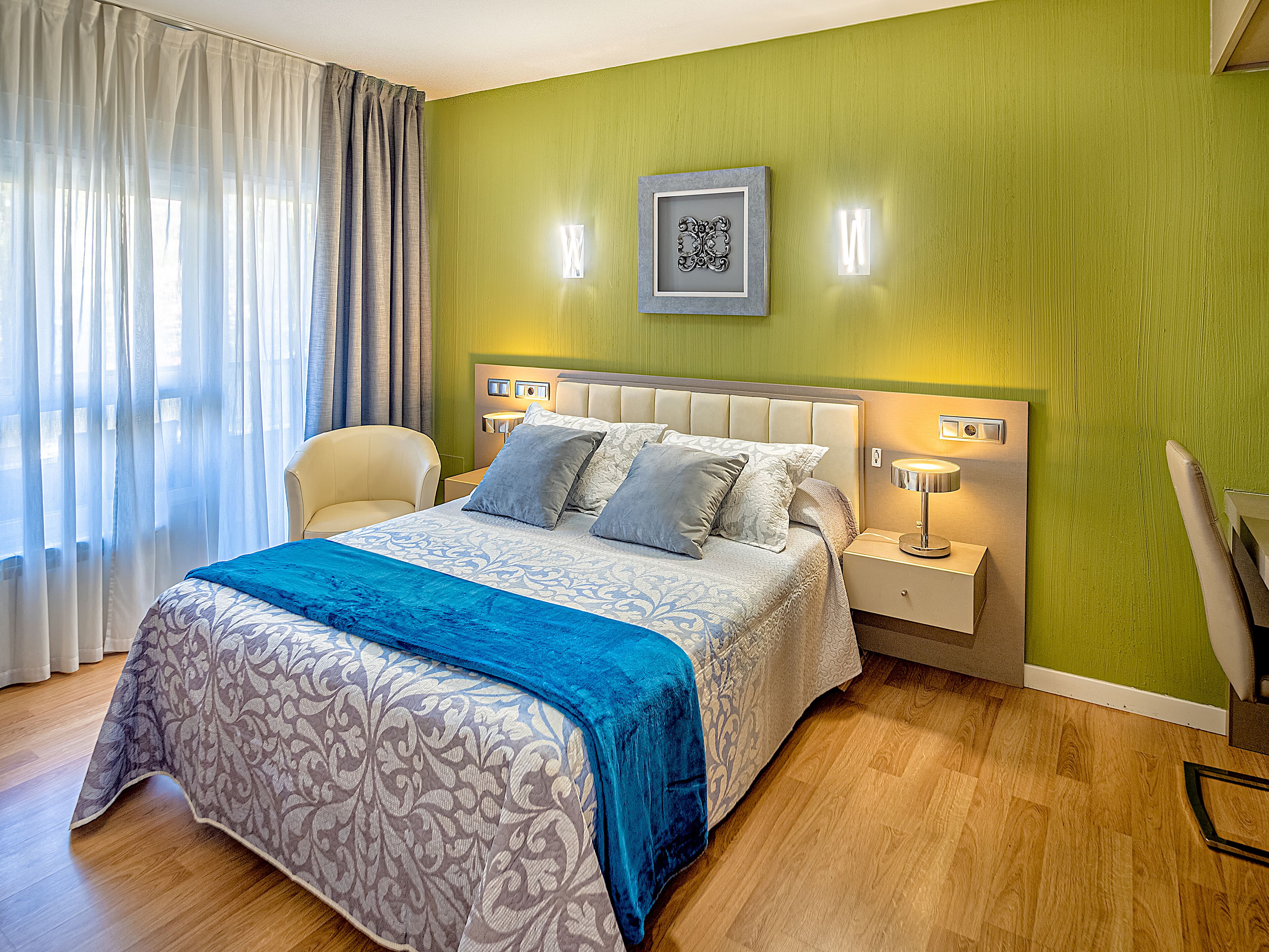 Un dormitorio ordenado con una cama, una silla y una mesita de noche con una lámpara.