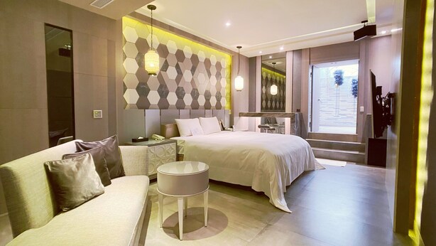 Een moderne hotelkamer met een groot bed, een bank, een klein rond tafeltje en een decoratieve wand met honingraatpatroon.