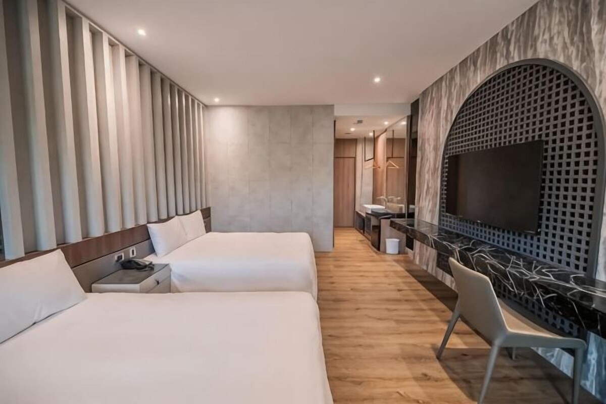 A hotel room with two beds, a desk, a chair, a TV, and a bathroom.