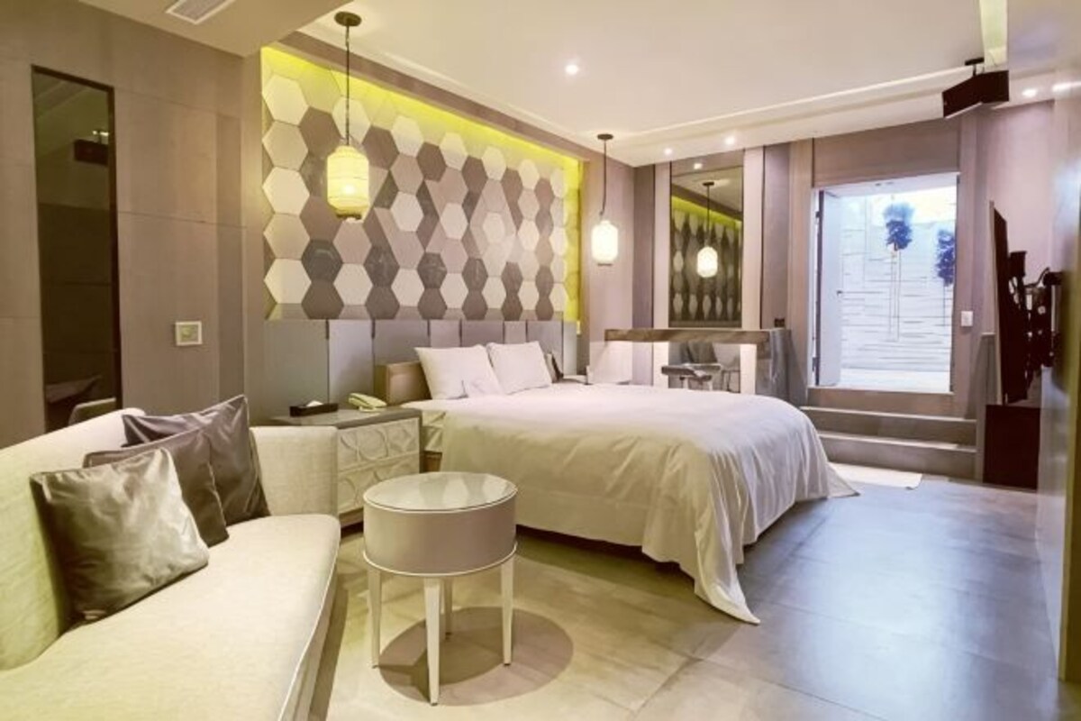 A modern bedroom with a bed, a sofa, a small round table, and a geometric patterned wall.