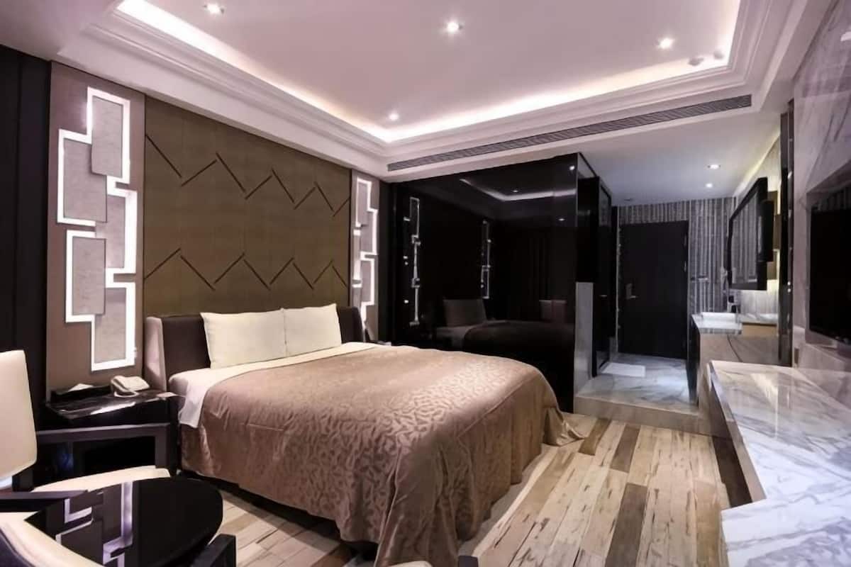A modern hotel room with a large bed, a desk, and a bathroom with a mirror.