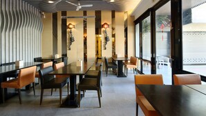 Een modern restaurantinterieur met hoge tafels en stoelen, decoratieve wandlampen en grote ramen.