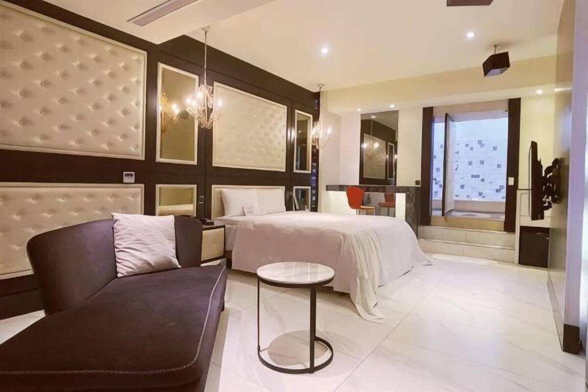 Una habitación de hotel moderna con una cama grande, un sofá, una mesita redonda y un ventanal con vistas.