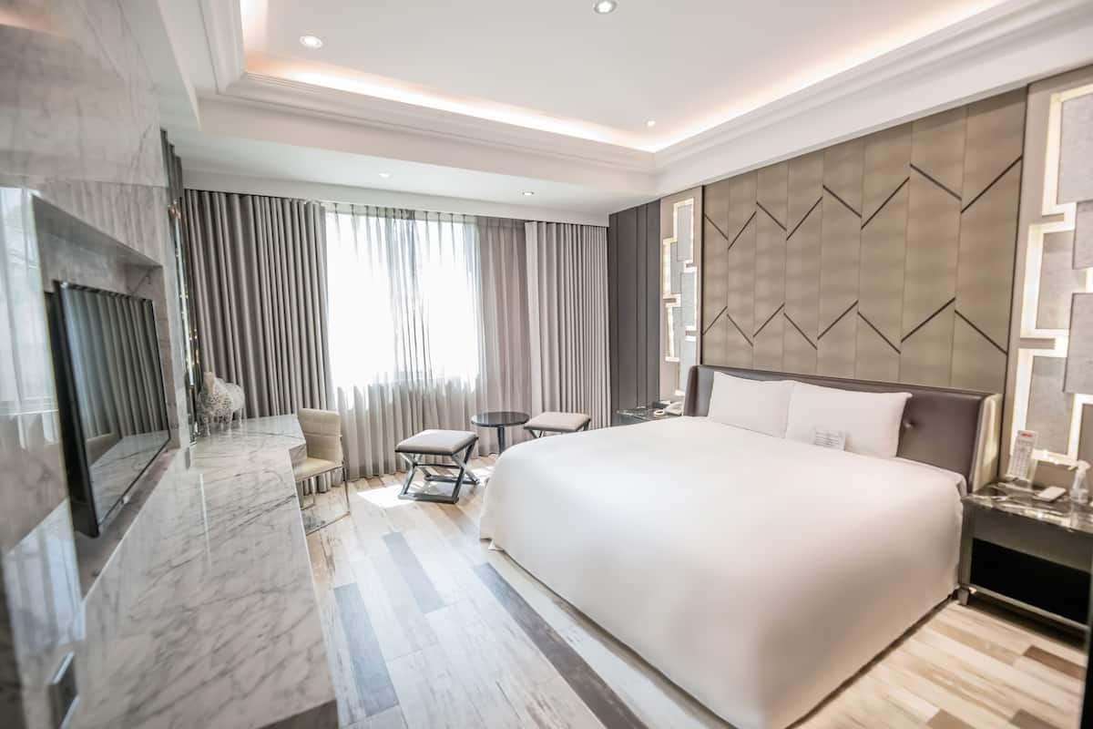 A modern hotel room with a large bed, a seating area with a small table, a TV, and a decorative wall panel.
