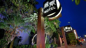 Een motelteken met een rond ontwerp en Chinese karakters, omgeven door tropische planten en een houten paal.