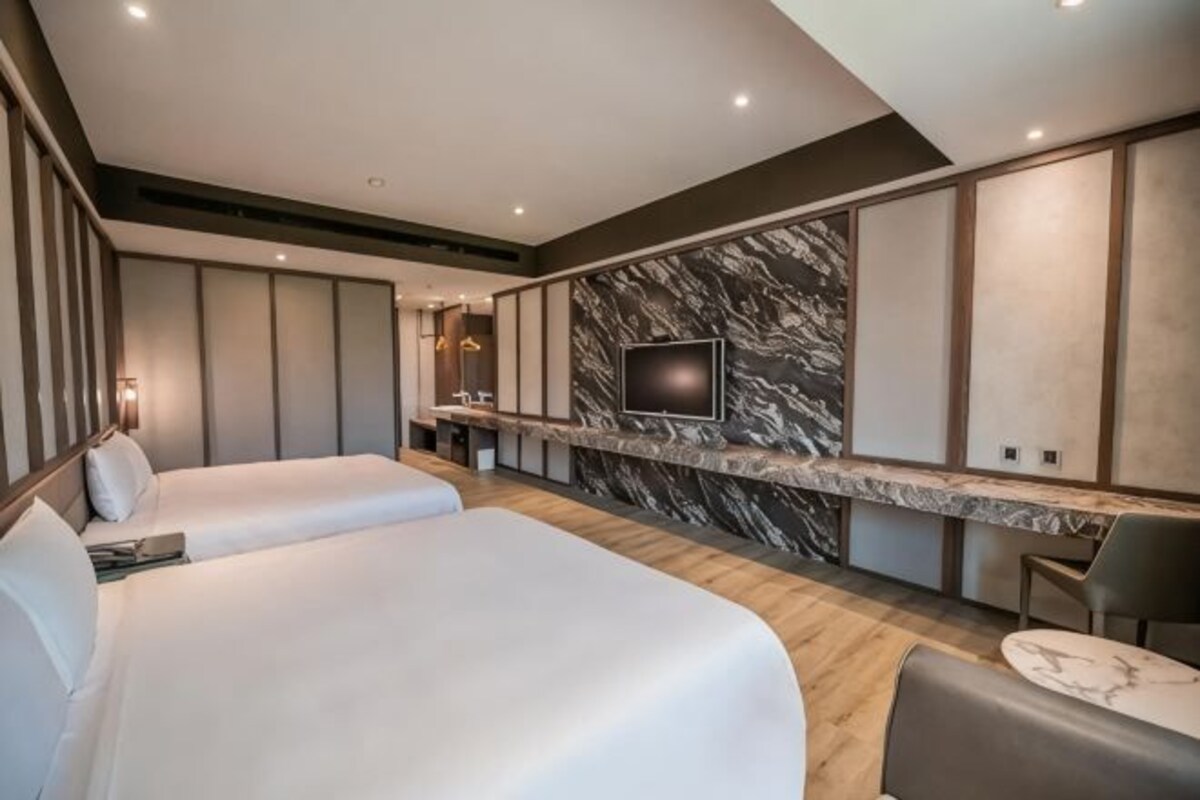 A hotel room with two beds, a marble accent wall, a TV, and a small seating area.