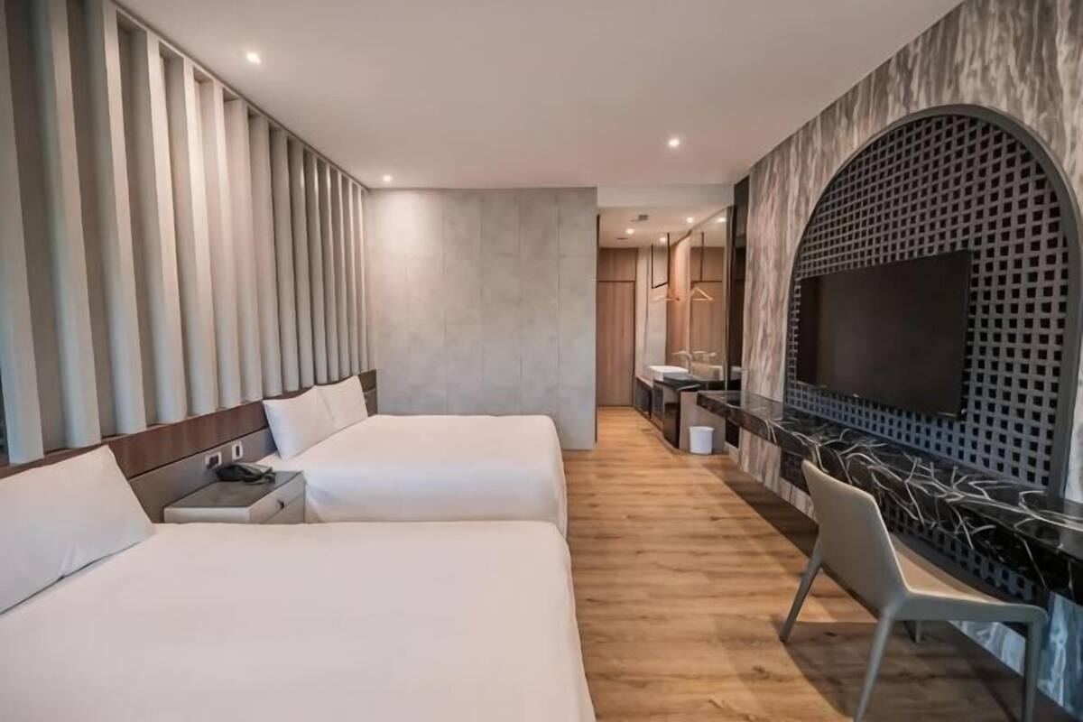 A hotel room with two beds, a desk, a chair, a TV, and a bathroom.
