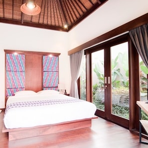 A bedroom with a large bed, a wooden ceiling, and a view of greenery outside.