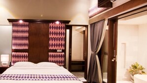 A modern hotel room with a large bed, a walk-in closet, a bathroom with a bathtub, and a ceiling with a patterned design. - Villa Puspa (Tabanan)