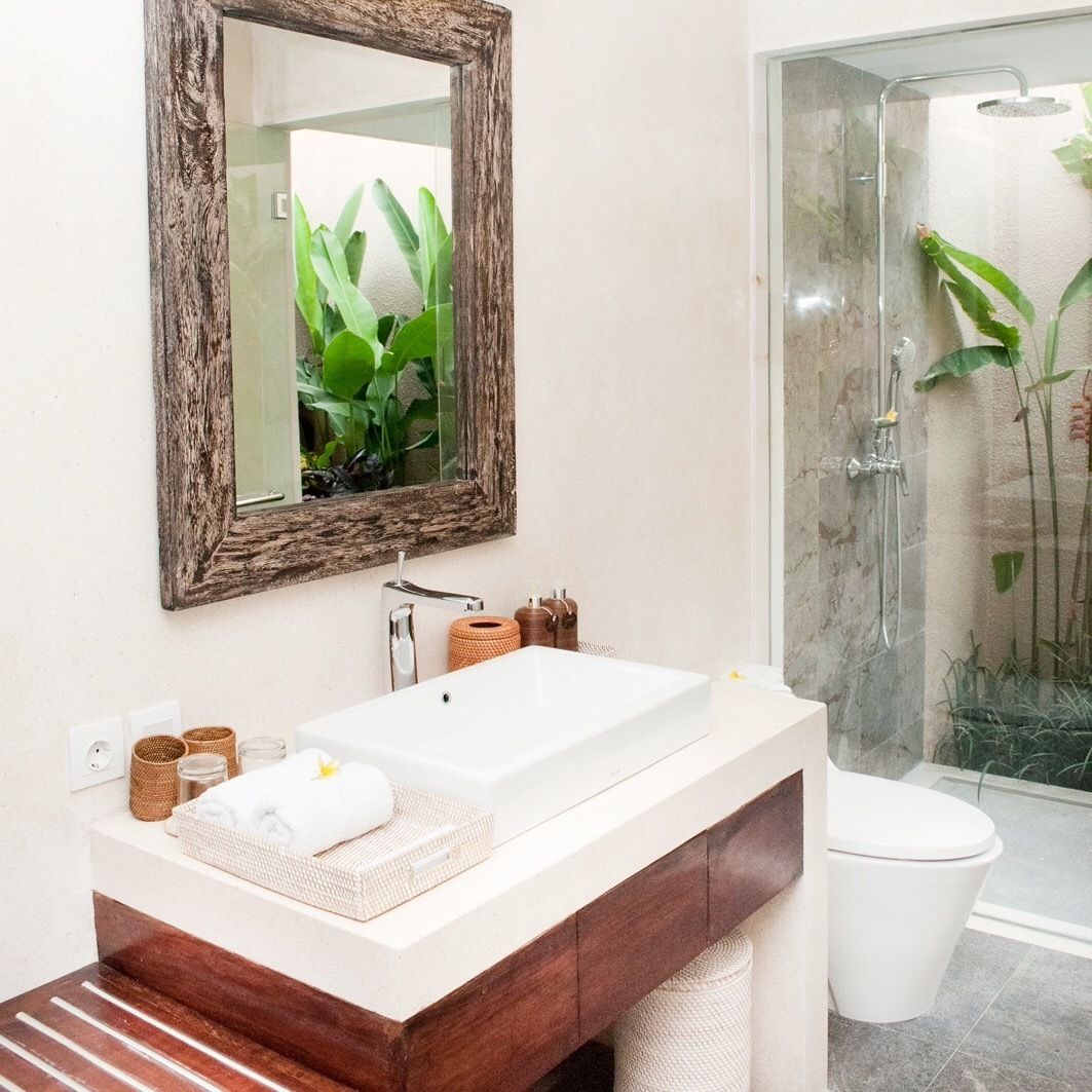 Un baño con un espejo grande, un lavamanos blanco, un tocador de madera y una cabina de ducha con mampara de cristal.