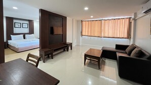 Une chambre d’hôtel moderne comprenant un lit, un téléviseur fixé sur un panneau en bois, un canapé, une table basse et une table à manger avec des chaises.