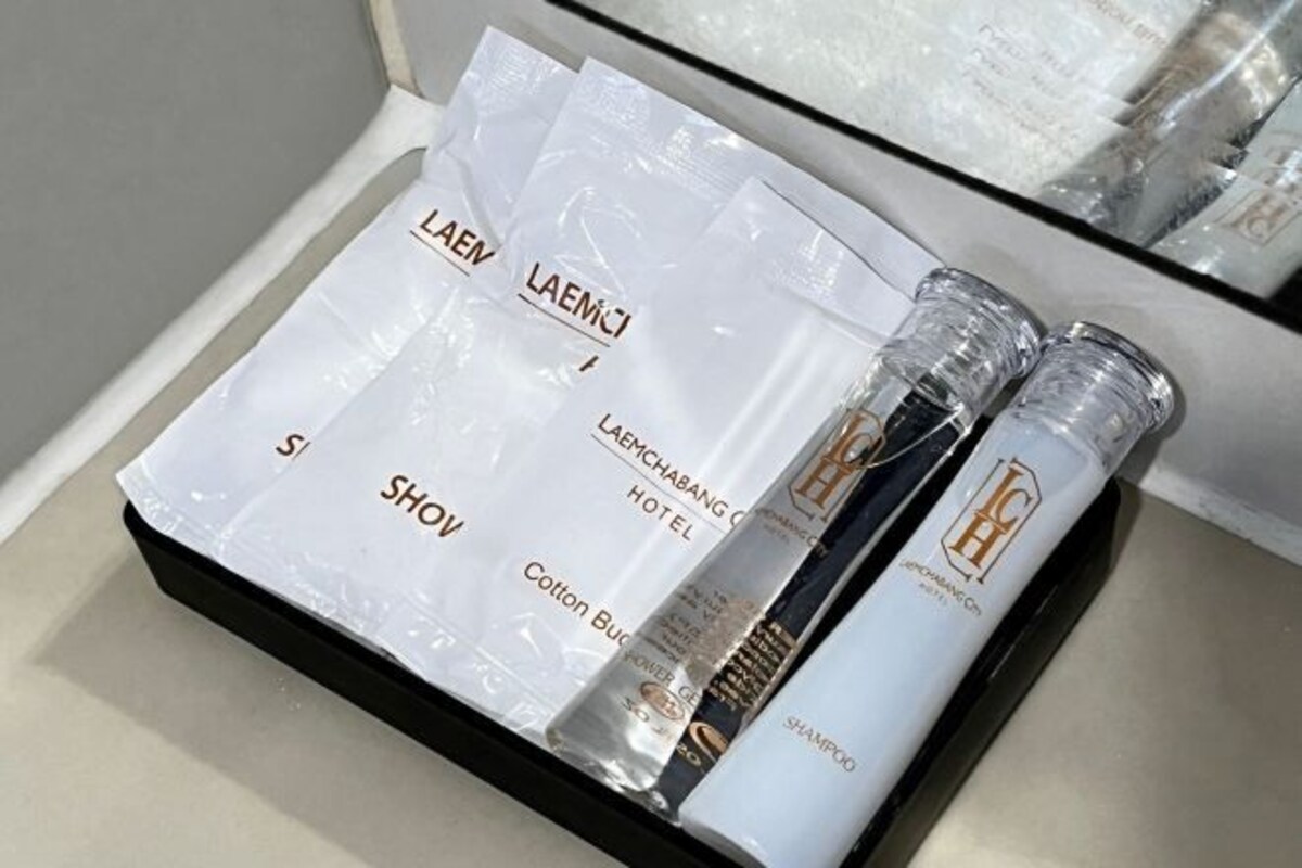 Une chambre d’hôtel avec un miroir à cadre noir, une table de chevet blanche et un ensemble de produits de toilette soigneusement disposés, comprenant une bouteille de shampoing et des cotons-tiges.