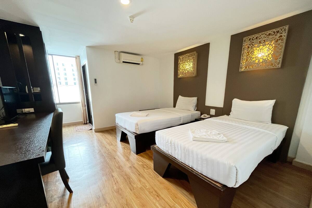 Een hotelkamer met twee eenpersoonsbedden, een bureau met stoel, een airconditioning en decoratieve wandpanelen.