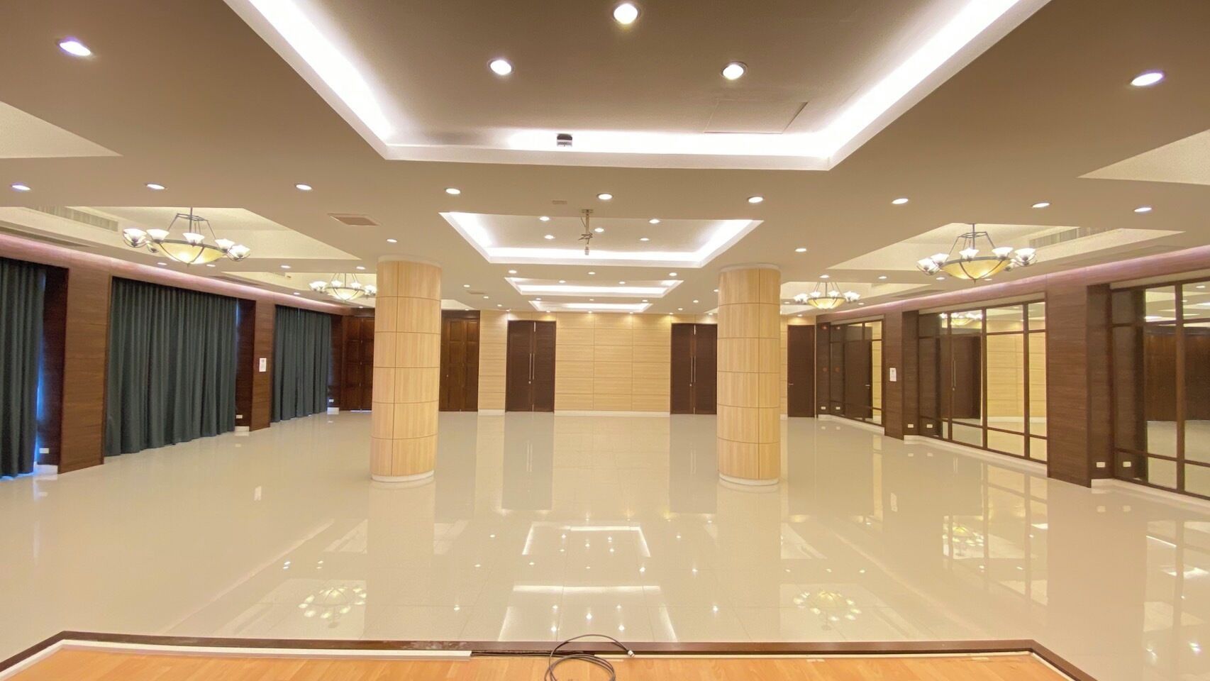A spacious, well-lit hotel lobby with a polished floor, large wooden pillars, and a modern chandelier.