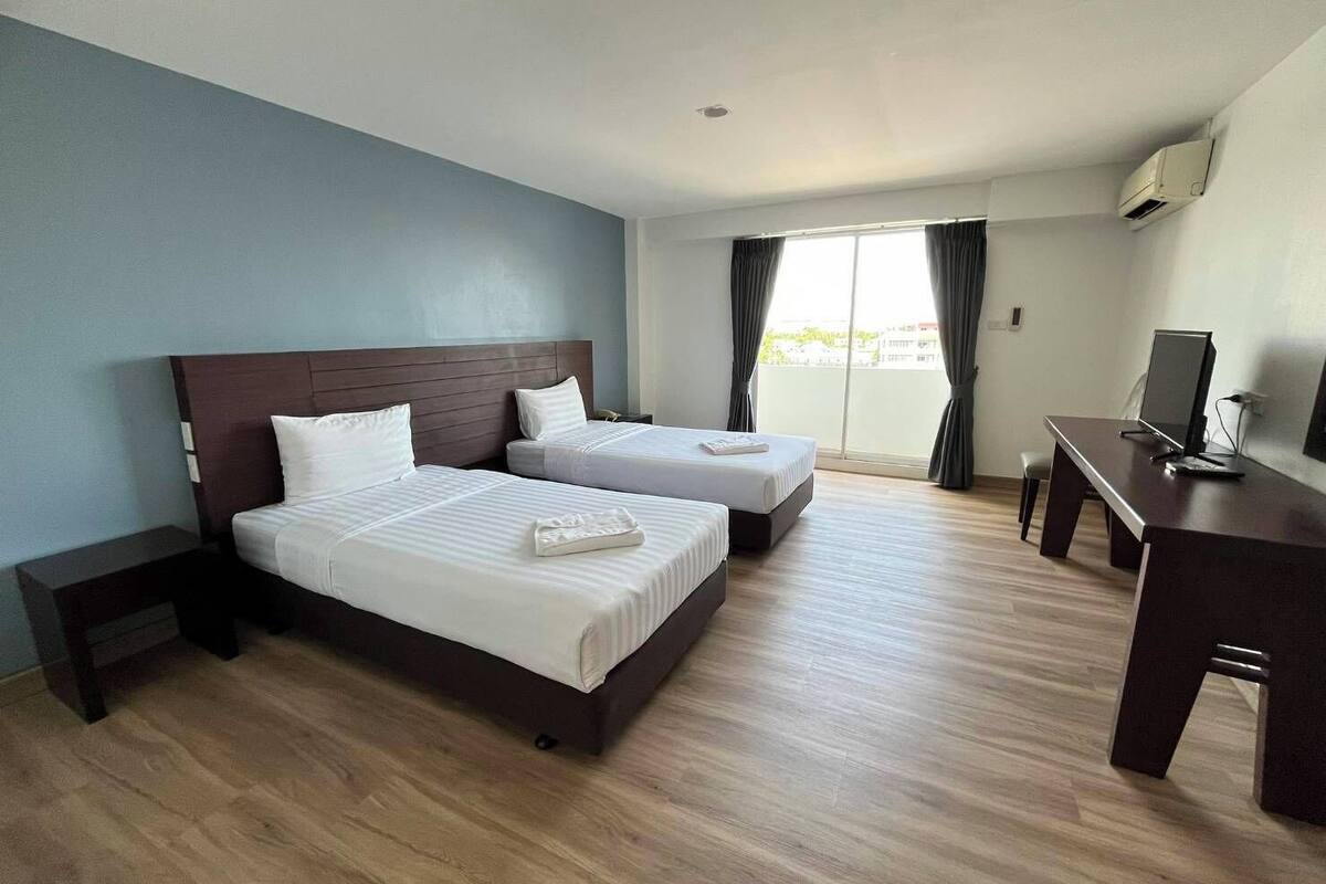Een hotelkamer met twee bedden, een bureau en een groot raam met gordijnen.