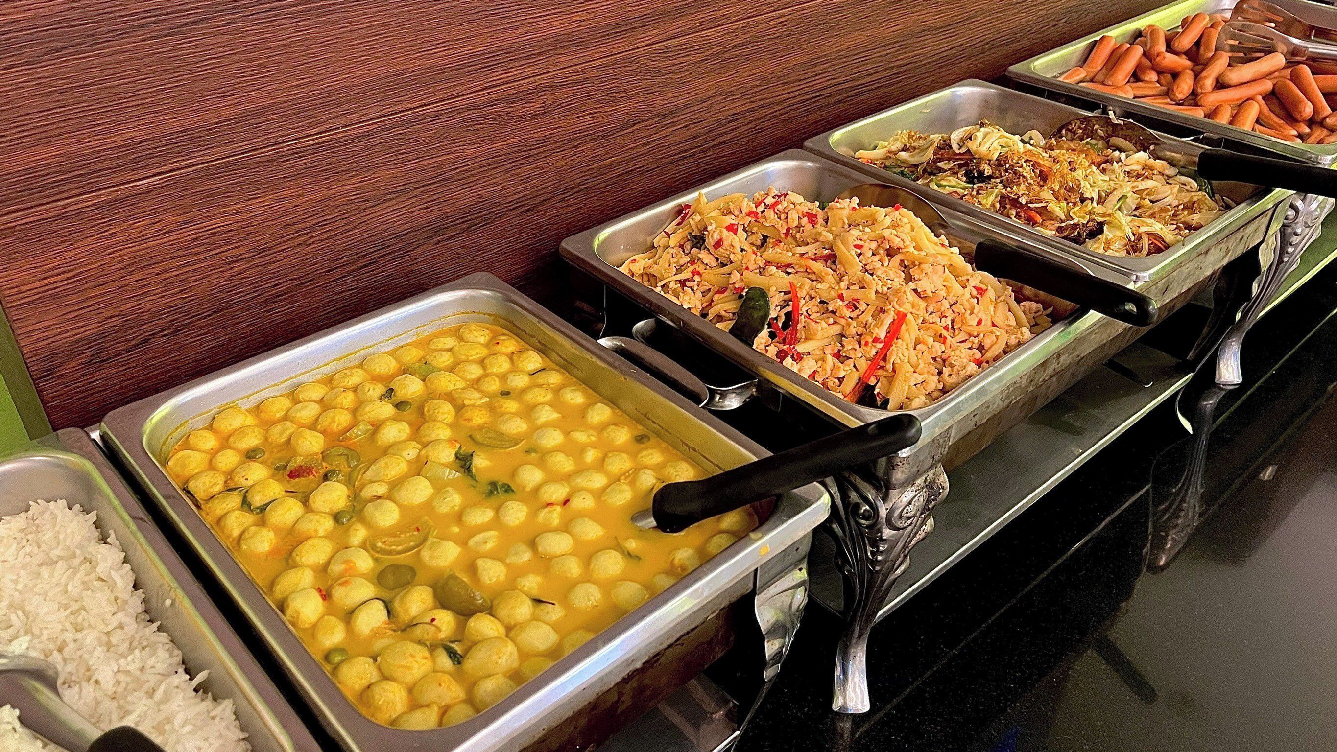 Un bufé con diversos platos, incluyendo arroz, un curry con bolitas amarillas, salteado de verduras y una bandeja de zanahorias.