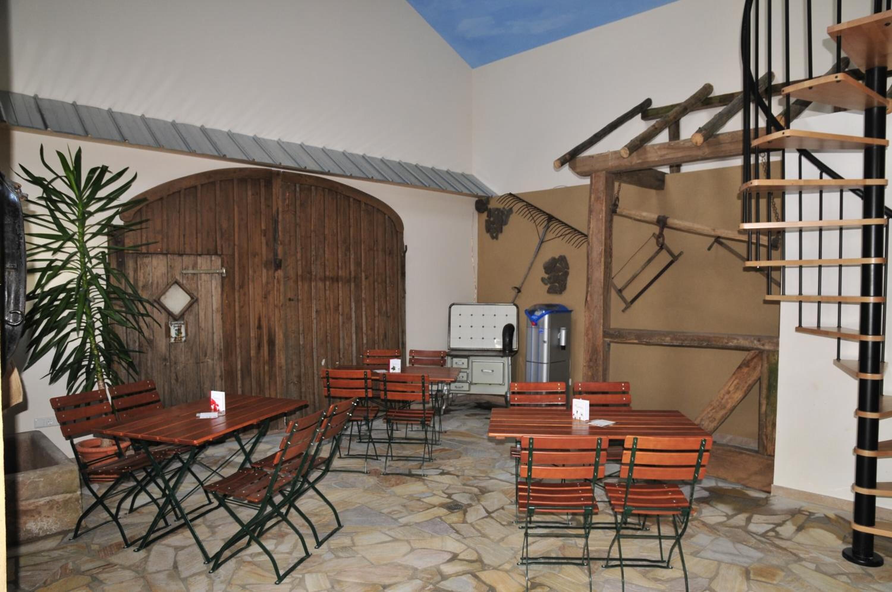 Ein Essbereich mit Holztischen und -stühlen, einem Steinfußboden und rustikaler Einrichtung, darunter eine Holztür und eine Wendeltreppe.