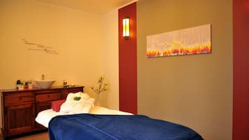 A bedroom with a bed, a wooden dresser, a wall-mounted light, and a painting.