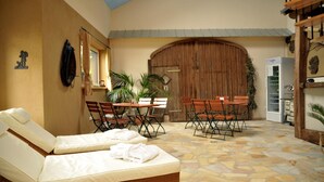 A sunlit room with a large wooden door, a dining table with chairs, a lounge area with two cushioned chairs, and a refrigerator. - Vulkanhotel Balance Selfness (Steffeln)
