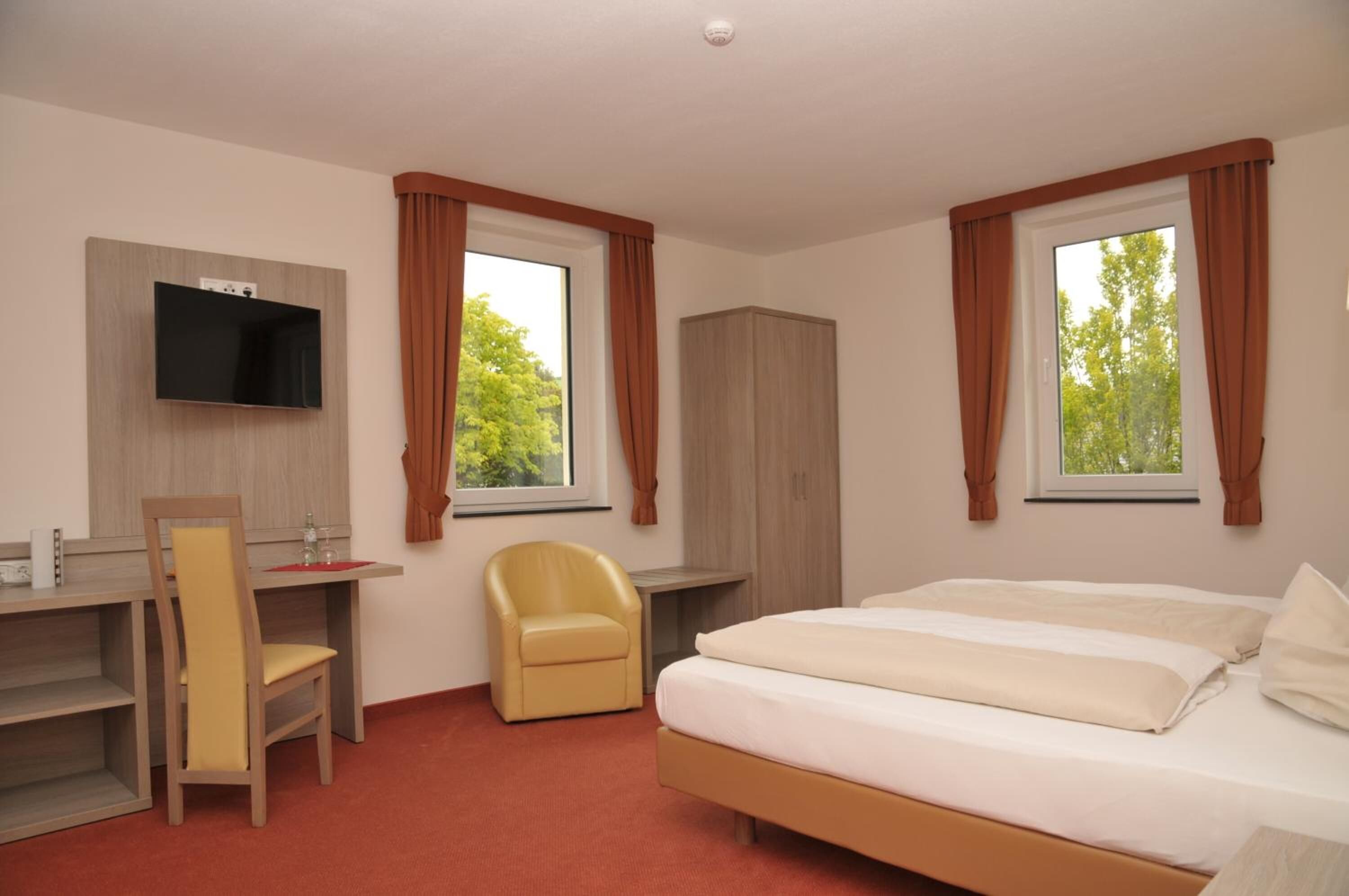 A hotel room with a bed, a desk, a chair, a TV mounted on the wall, and a wardrobe.
