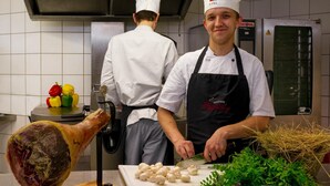 A chef preparing food in a kitchen with a large meat carving stand and fresh vegetables on the counter. - Vulkanhotel Balance Selfness (Steffeln)