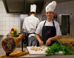Un chef preparando comida en una cocina con un gran carro de despiece de carne y verduras frescas en la encimera.