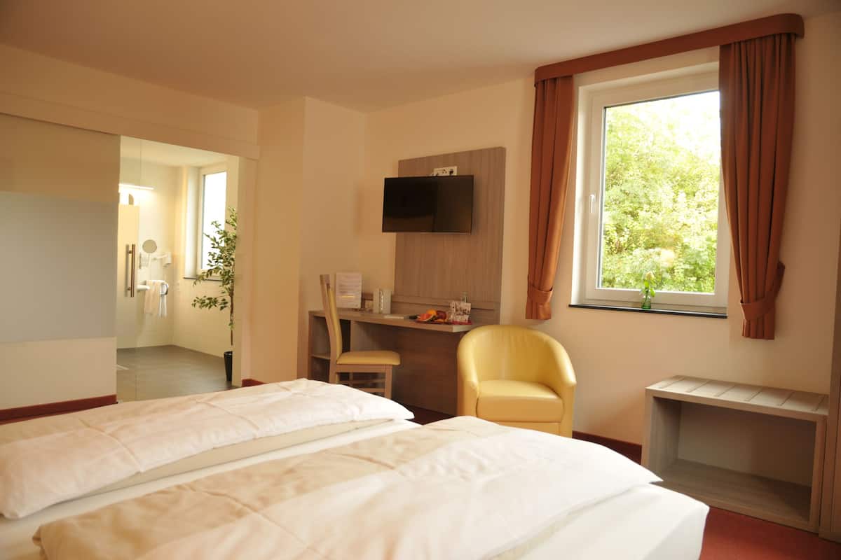 Une chambre d’hôtel avec deux lits, un bureau, une chaise, un téléviseur fixé au mur et une fenêtre avec des rideaux.