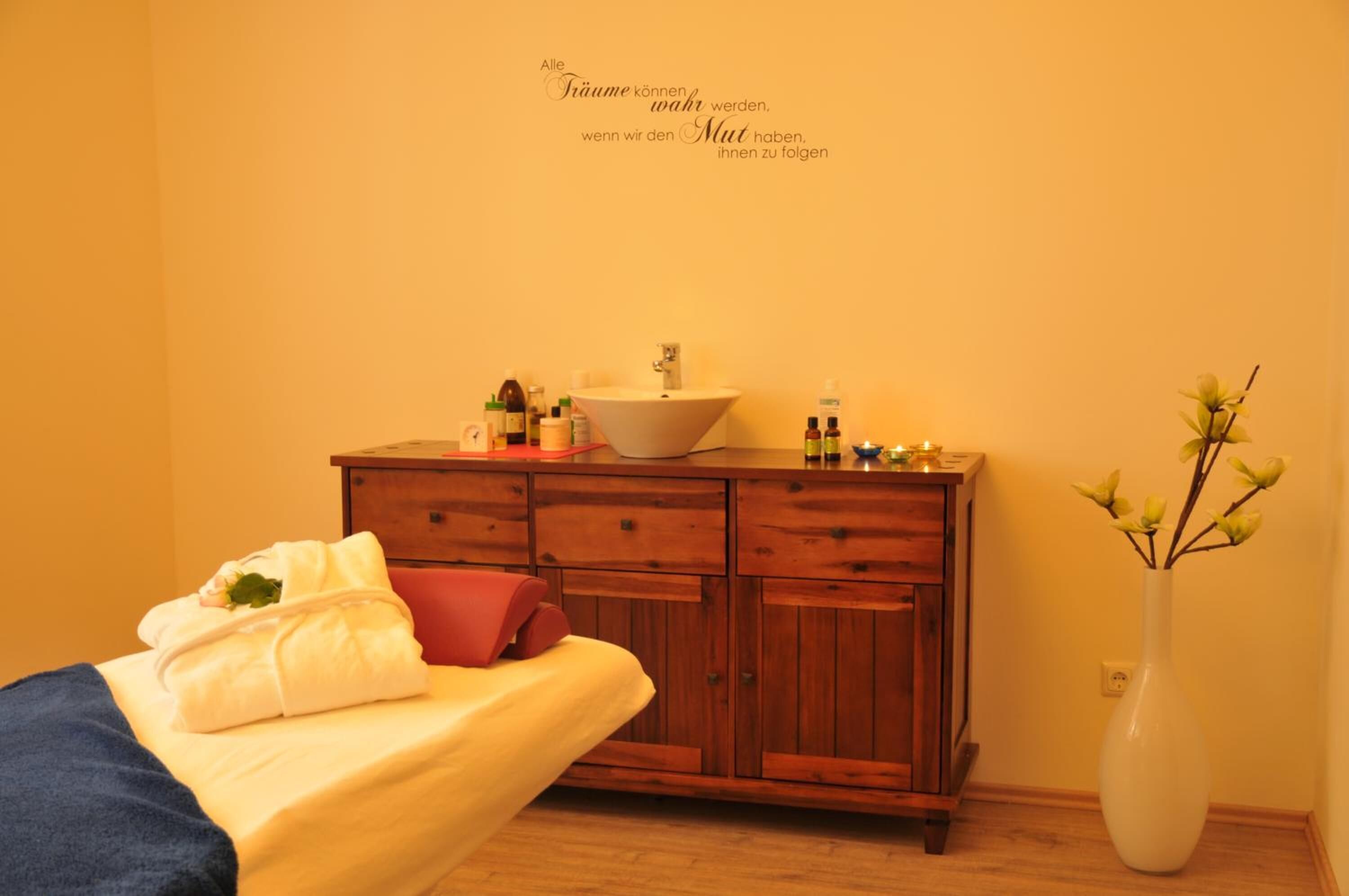 Quarto de hotel com cômoda de madeira, cama com colcha amarela e um vaso com flores.