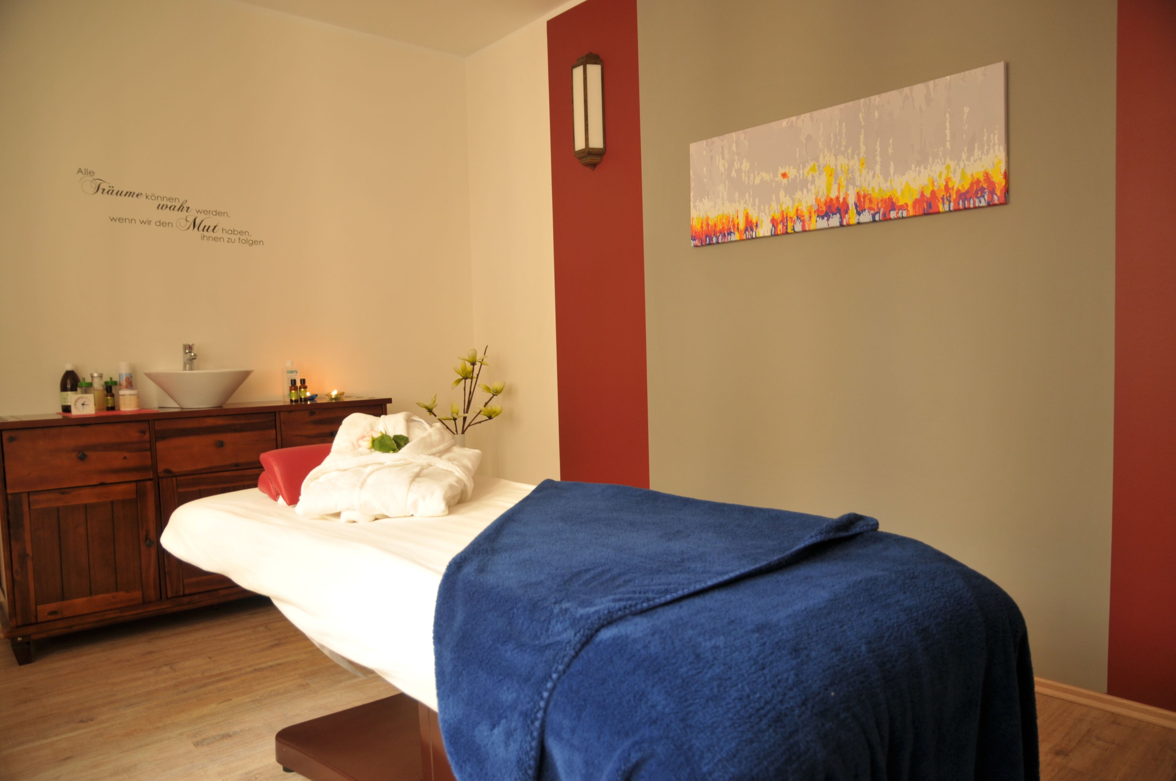 A room with a bed, a wooden cabinet, a sink, and a wall with a painting.